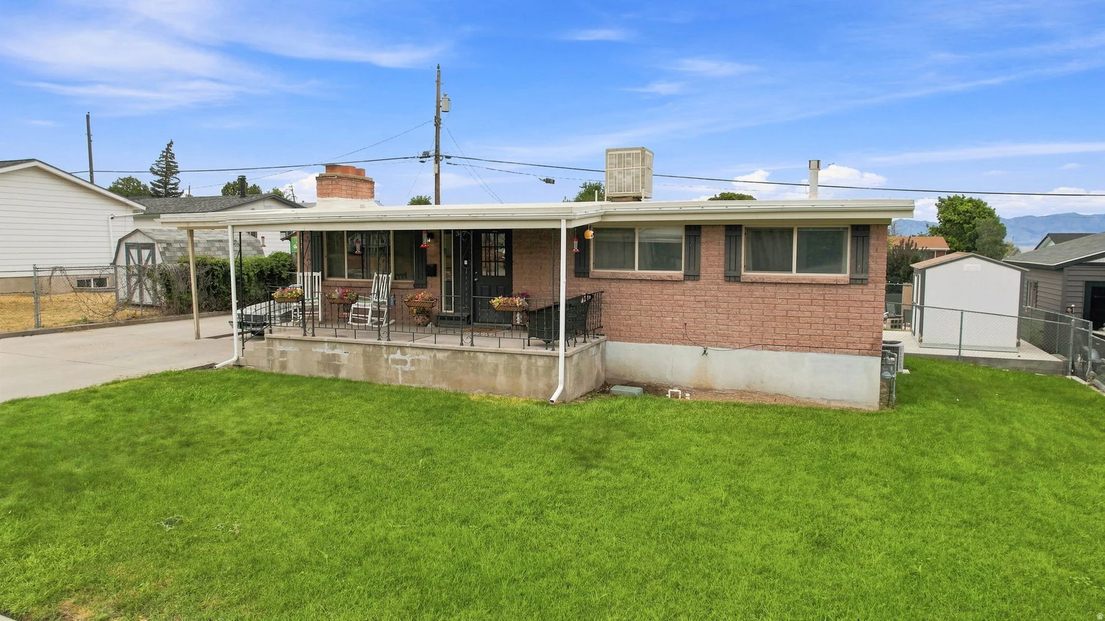 Brick exterior, covered front porch, carport, mature landscaping, and an external storage shed